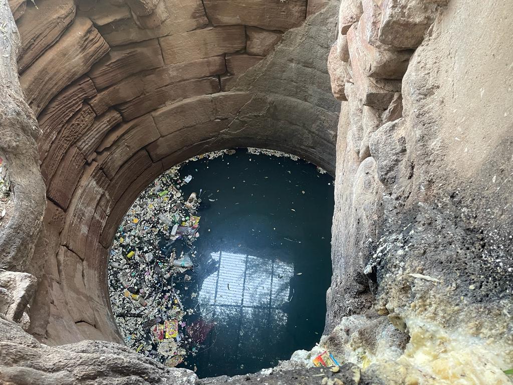 the image is of the well where people pour ghee. some trash is also in the water and the circular marks of the brown stone are also present.