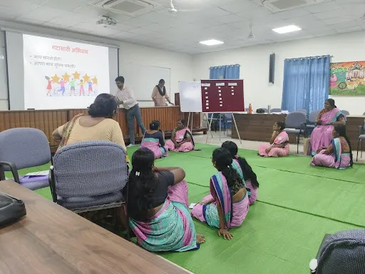 Aanganwadi workers in knowledge sharing, in a classroom where a trainer (male) is projecting a presentation