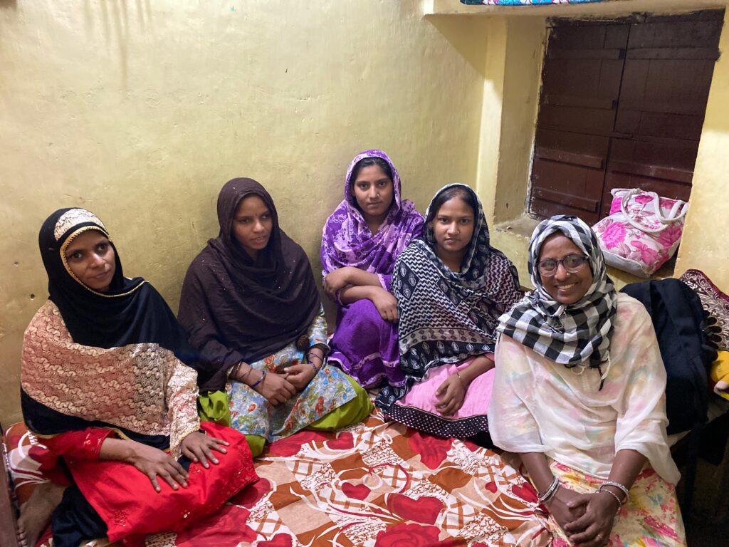 Five women are sitting and smiling and looking at the camera.