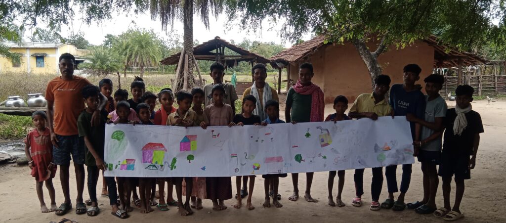 Several children stand in line displaying the paper strip they have painted. There are a few men with them as well. Behind are green trees.
