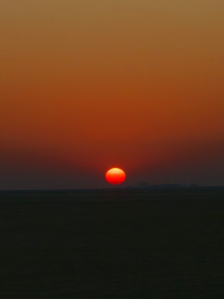 A portrait of sunset with orange sun and orange skies and dark ground.